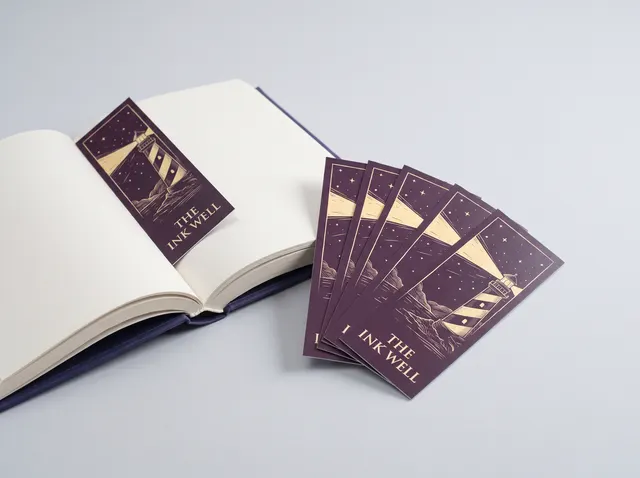 Plum The Ink Well bookmarks with a gold lighthouse illustration, one tucked in a book