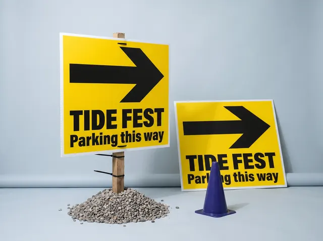 Yellow Tide Fest parking signs on Correx, one tied to a stake in gravel