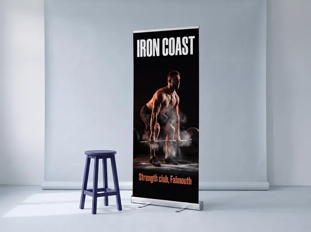 An Iron Coast gym roller banner with an athlete mid-lift in chalk dust, on a slim cassette with its swing-out feet pulled out