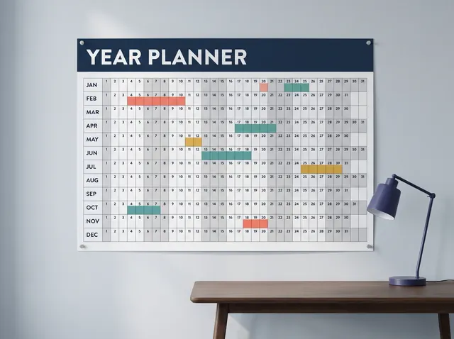 An A1 year planner pinned to the wall above a desk, with coloured bookings